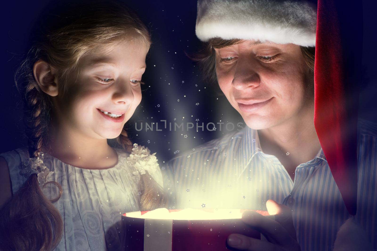 father in Santa Claus cap and daughter opened a box with Christmas gift boxes of shining light and magic