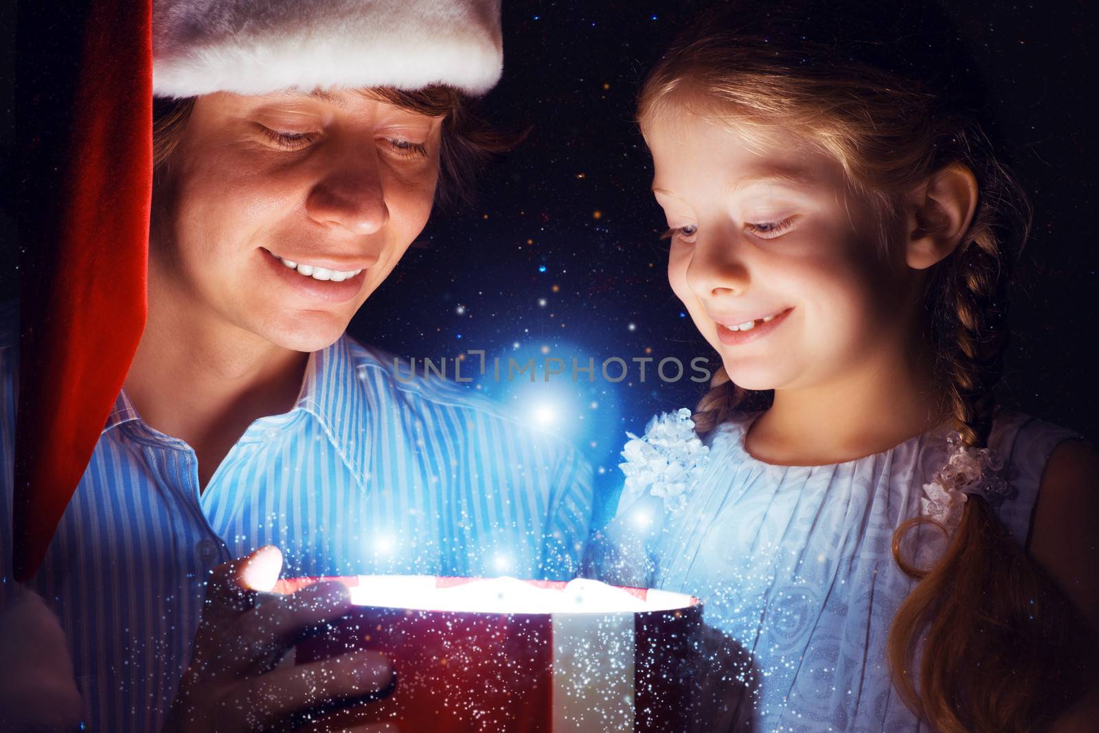 father in Santa Claus cap and daughter opened a box with Christmas gift boxes of shining light and magic