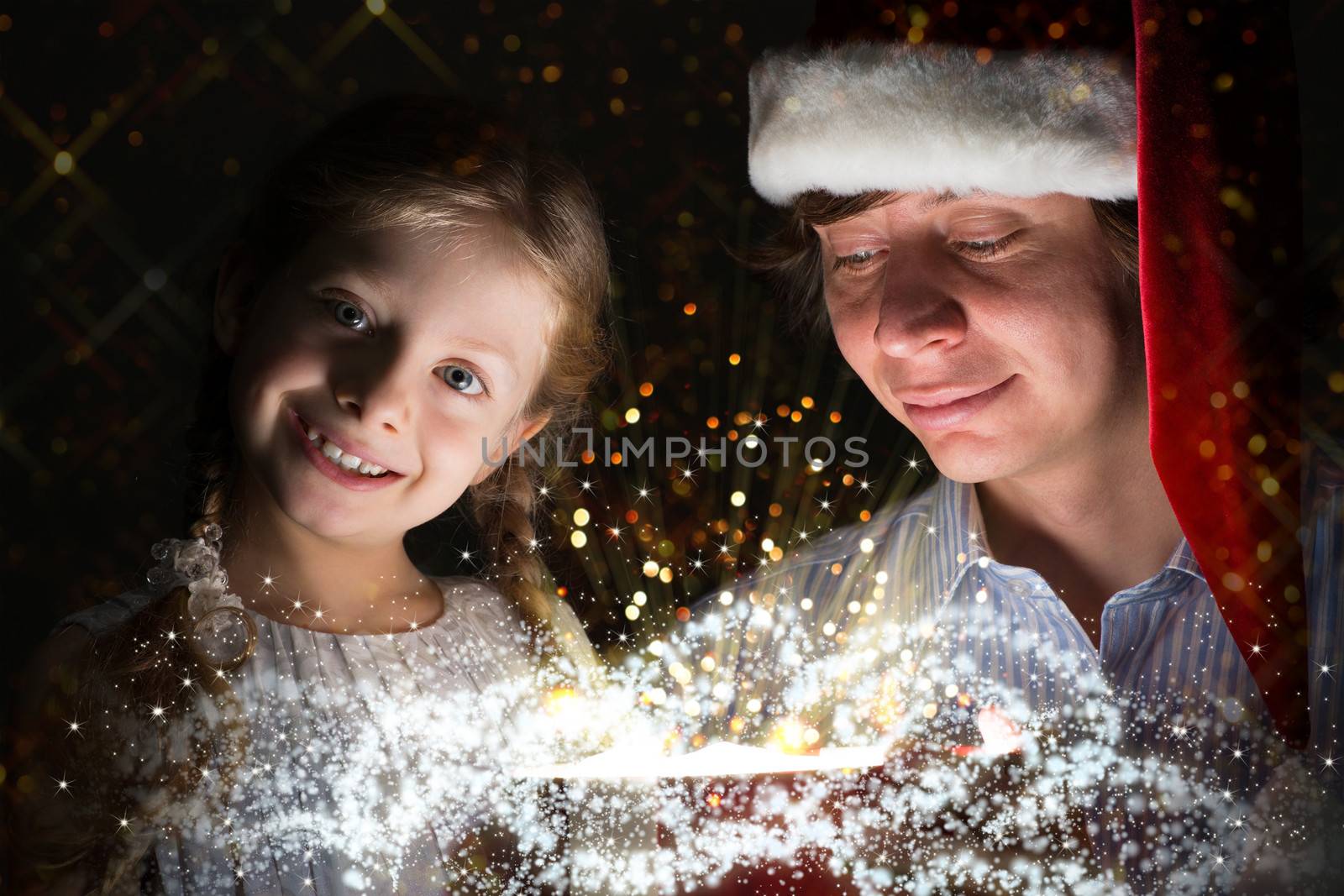 father in Santa Claus cap and daughter opened a box with Christmas gift boxes of shining light and magic