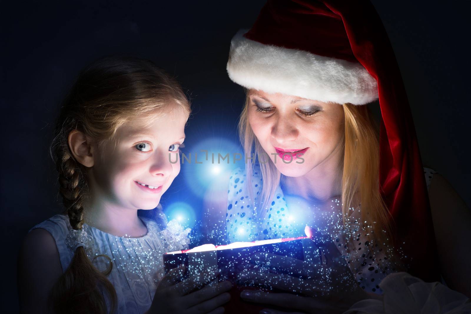 mother in Santa Claus cap and daughter opened a box with Christmas gift boxes of shining light and magic