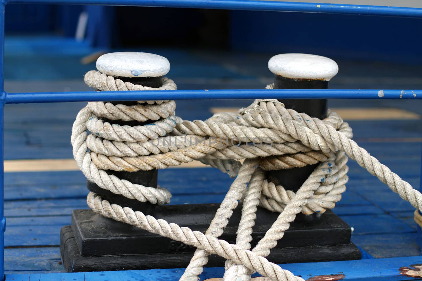 Close-up of a mooring rope with a knotted end tied around a cleat on a wooden pier/ Nautical mooring rope