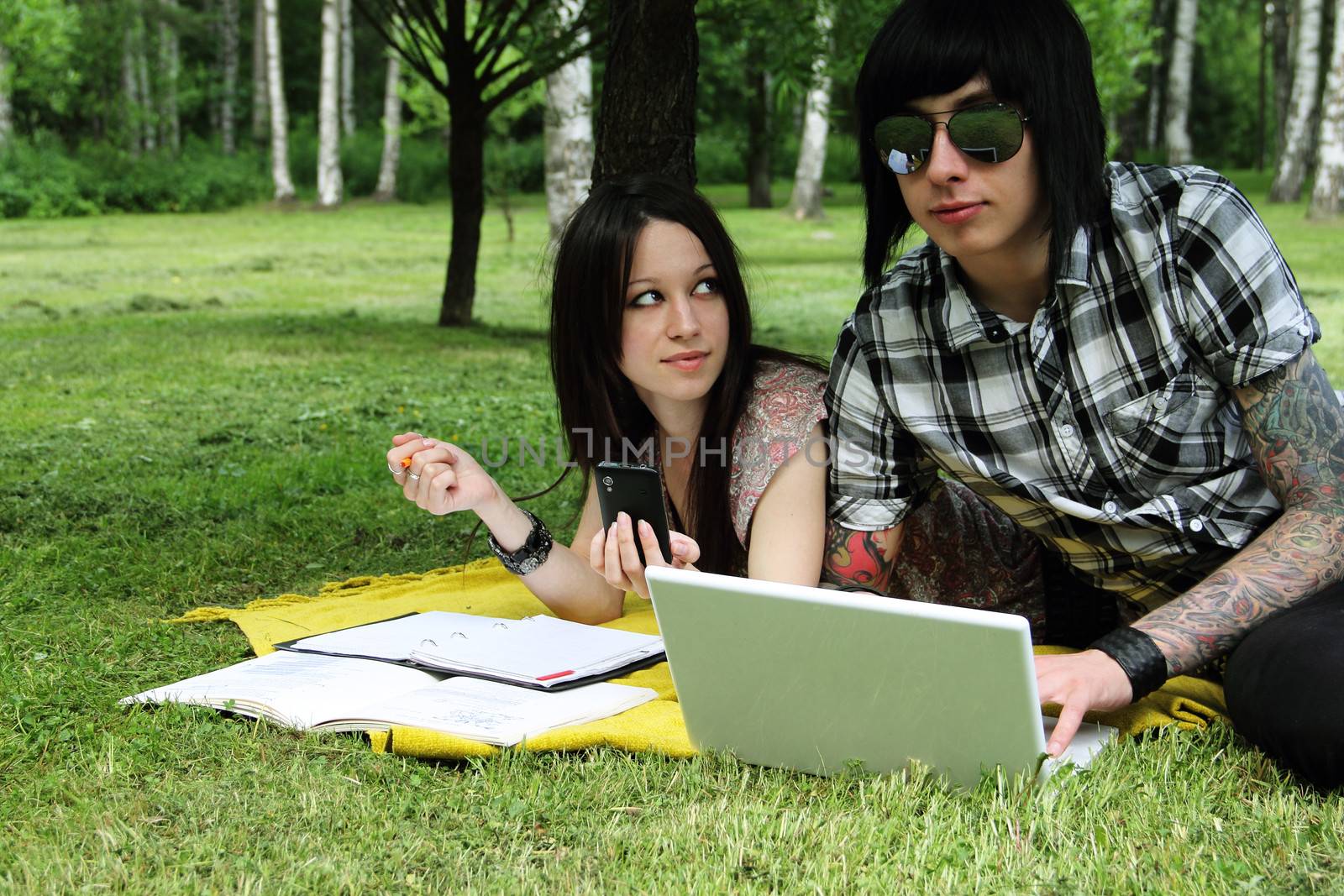 Couple of young students studying outdoors with laptop and books