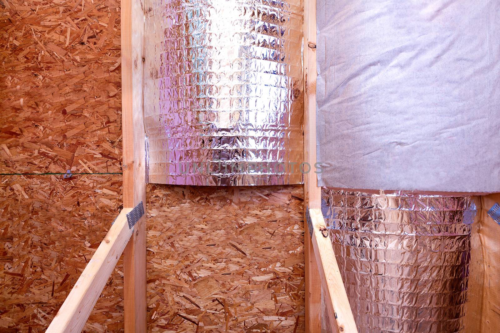 Attic insulating with reflective heat barrier and fiberglass cold barrier between the attic joists, work is ongoing, inside gable and joist view