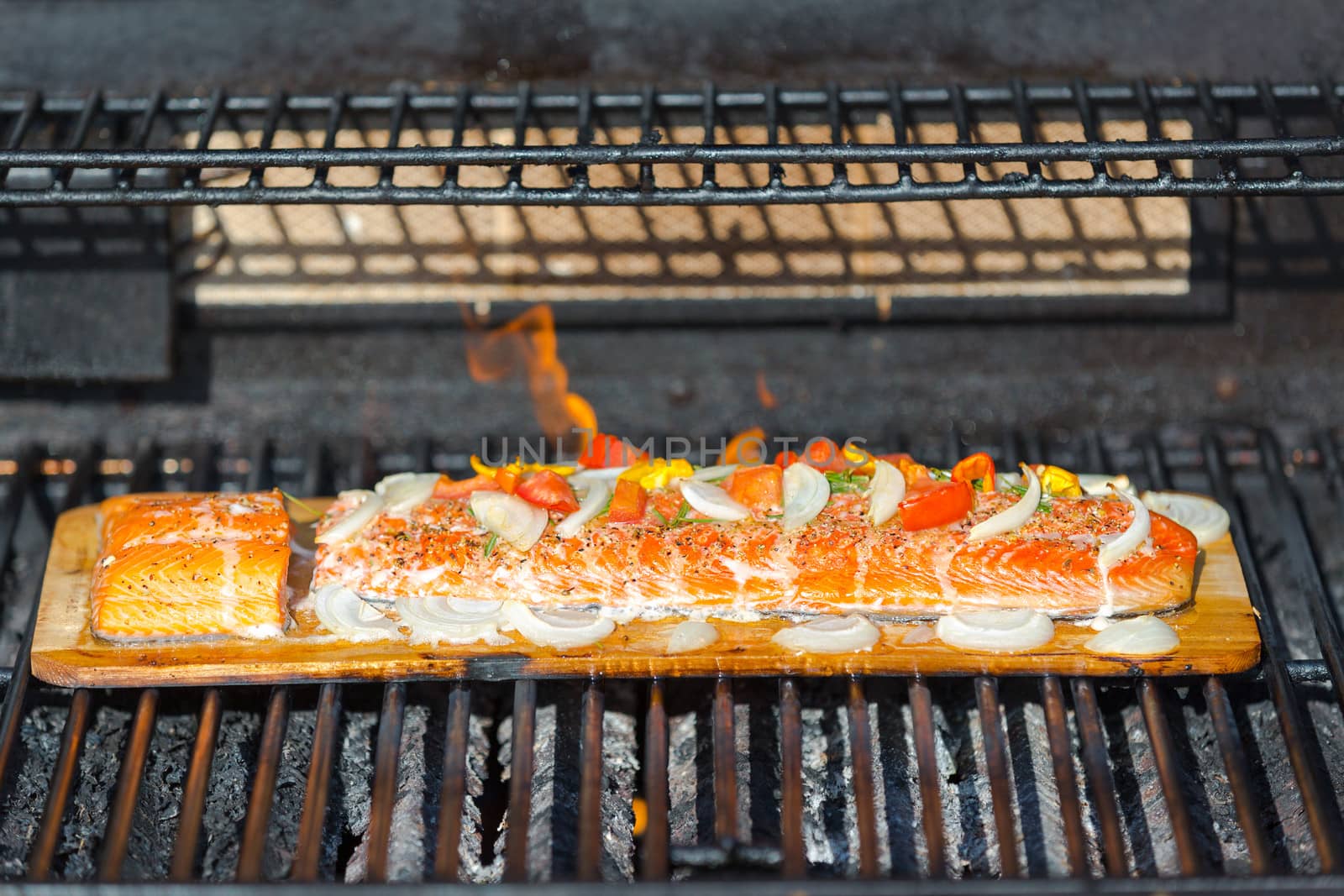 Cooking salmon on cedar plank in the barbecue, garnished with onions, tomatoes, dill and herbal seasonings