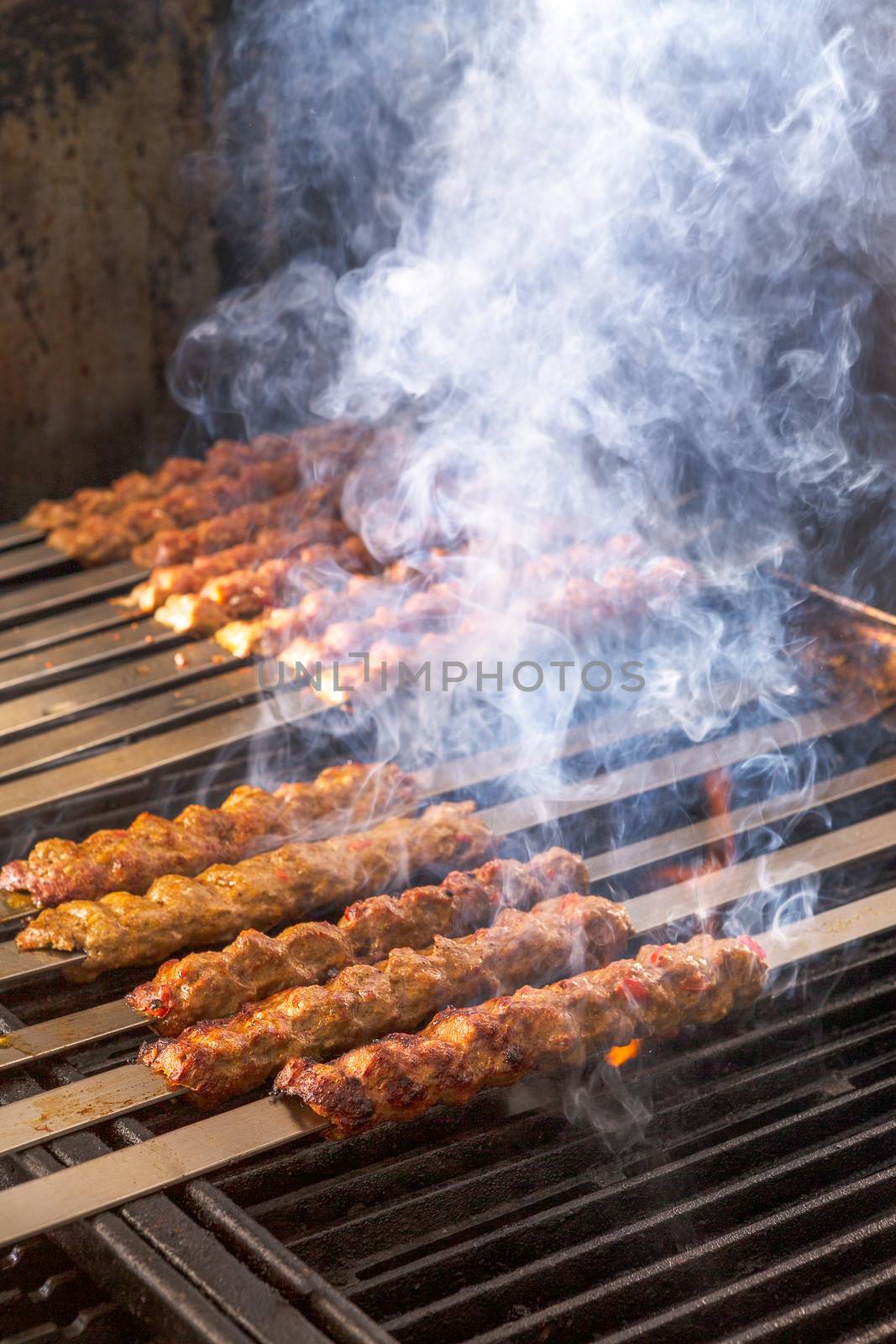 Cooking Adana kebabs on the restaurant style grill, smoke  coming out from them that they might be ready