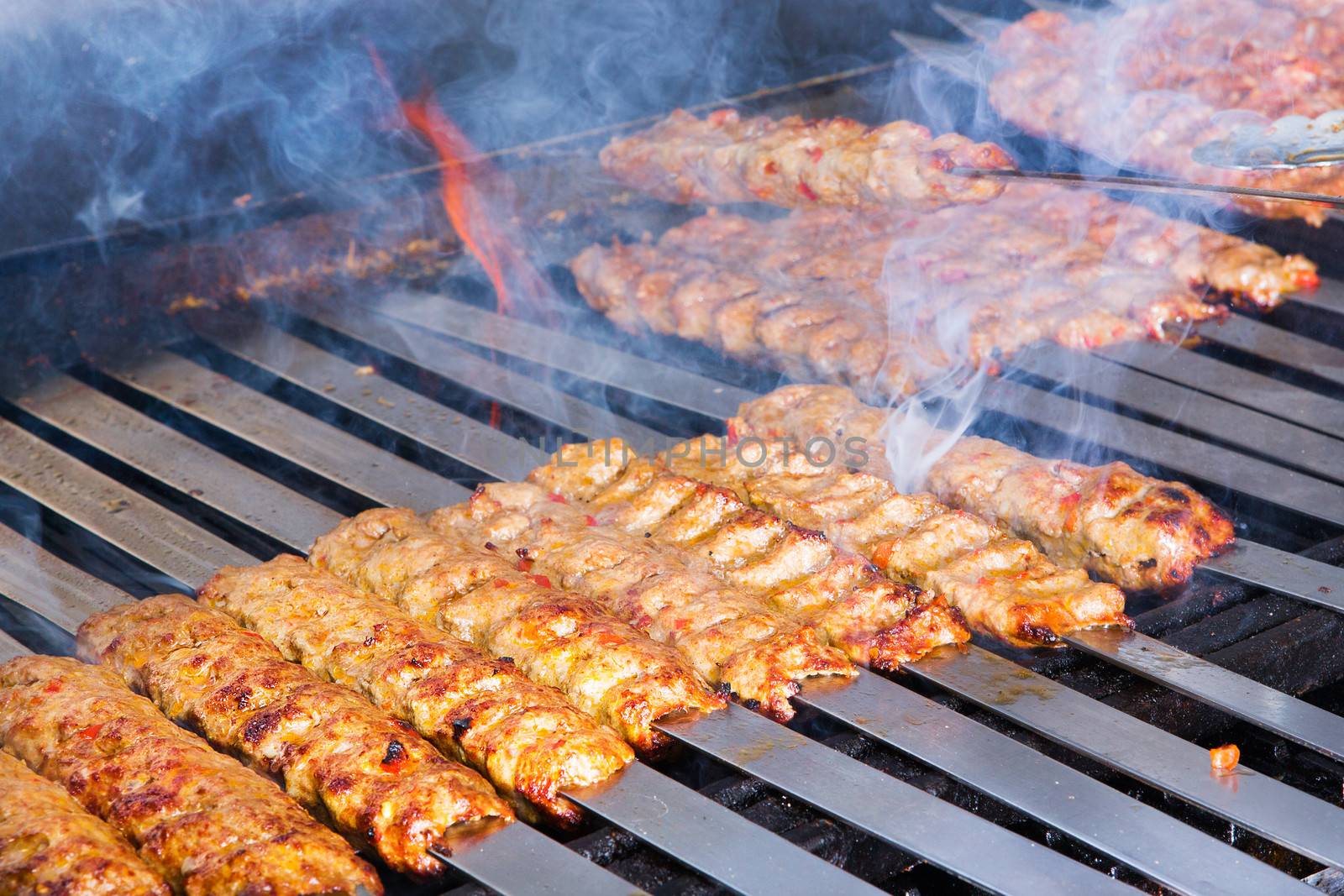 Cooking Adana kebabs on the restaurant style grill, smoke  coming out from them that they might be ready