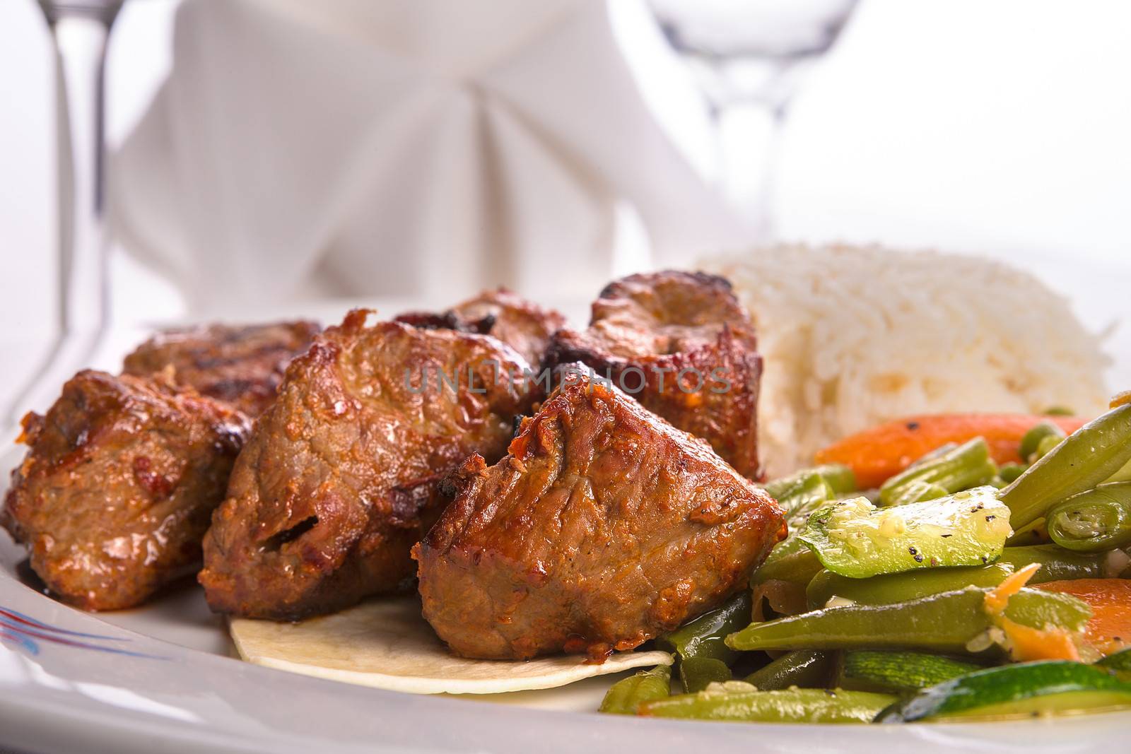 Macro shot of shish kebabs garnished with vegetables and rice pilaf, napkin and vine glass on the background