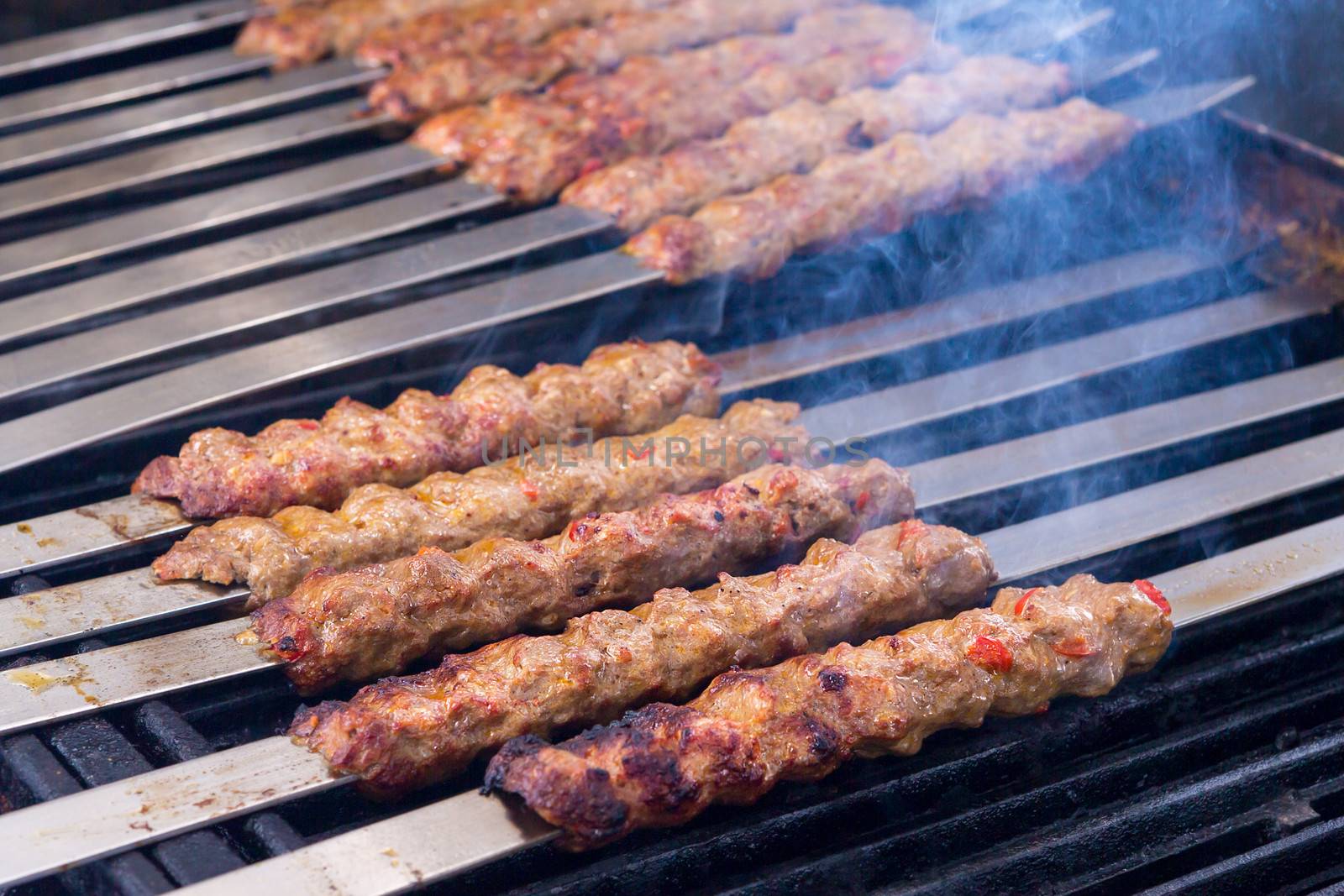 Cooking Adana kebabs on the restaurant style grill, smoke  coming out from them that they might be ready