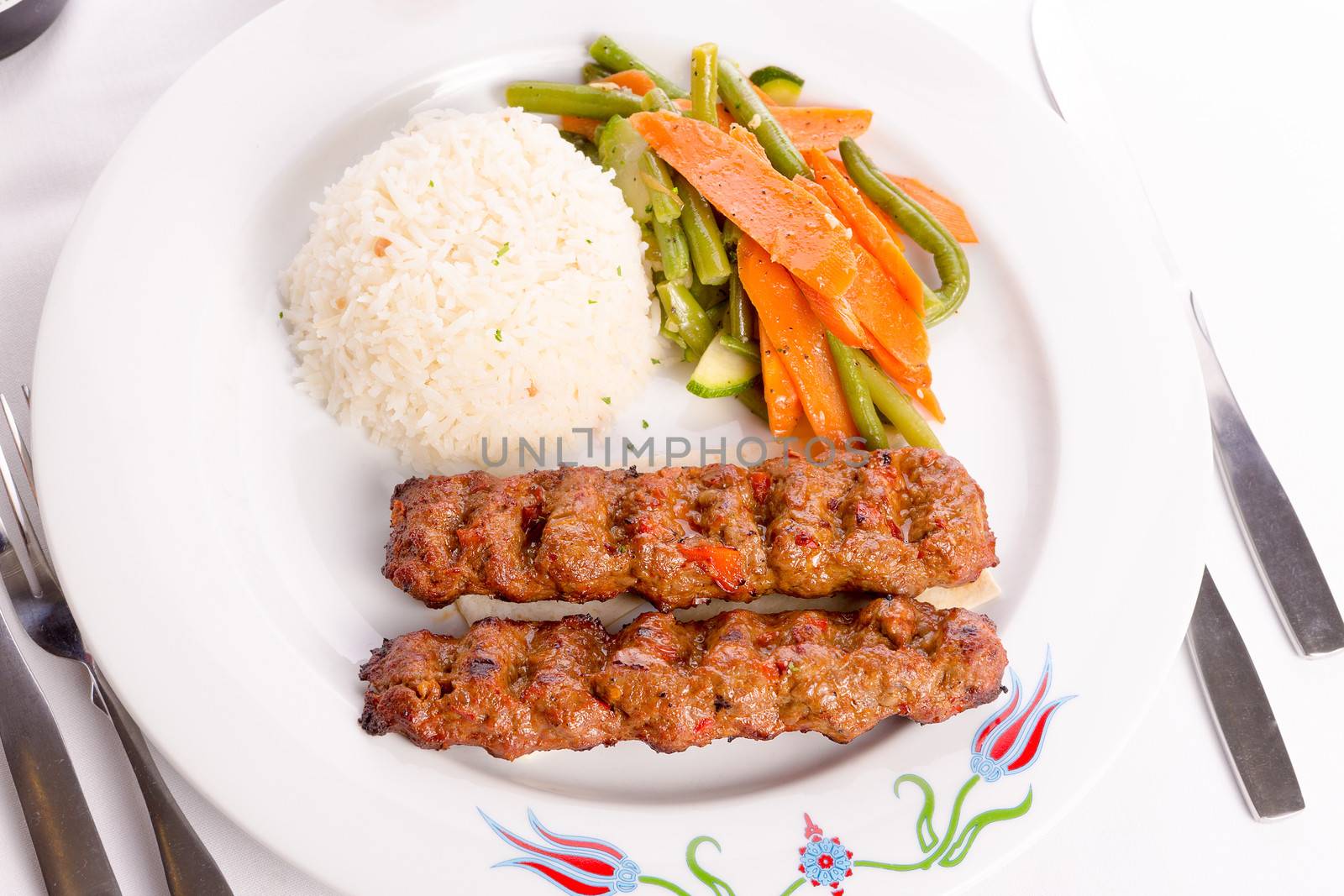 Turkish Adana Kebap with rice pilaf and vegetables served on a Plate