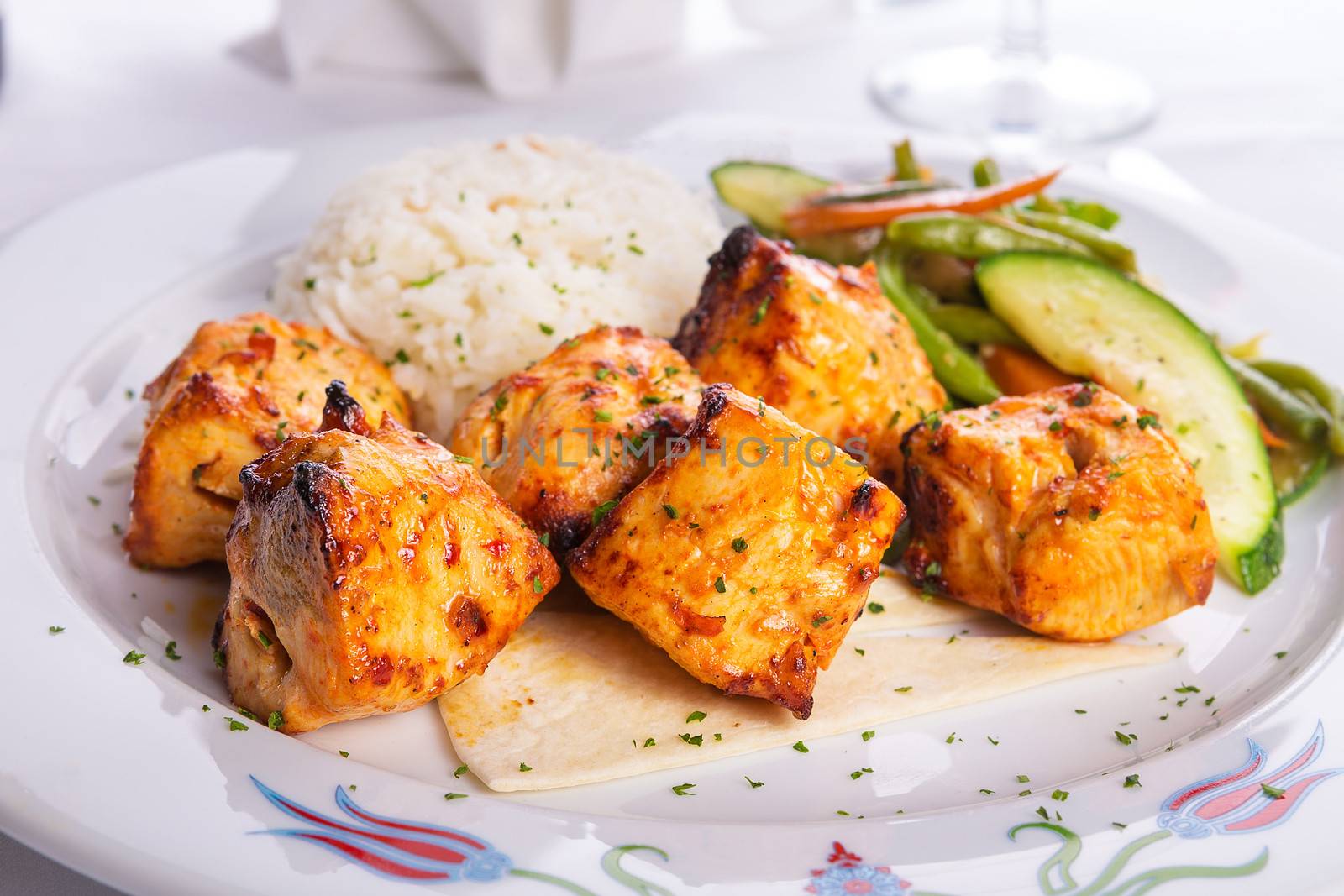 Zesty chicken shish kebabs served with rice pilaf on a tiny lavash bread garnished with cooked vegetables zucchini, green beans and carrots