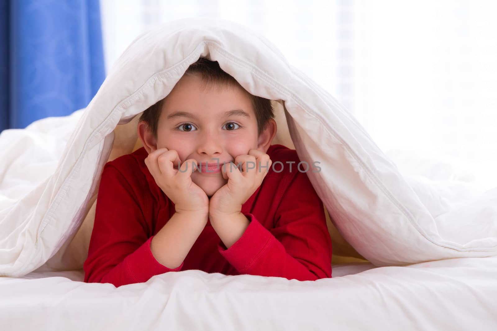 Close up portrait of a eight years old boy laying on the bed on looking at  you in his bedroom at home. He looks calm and relaxed.