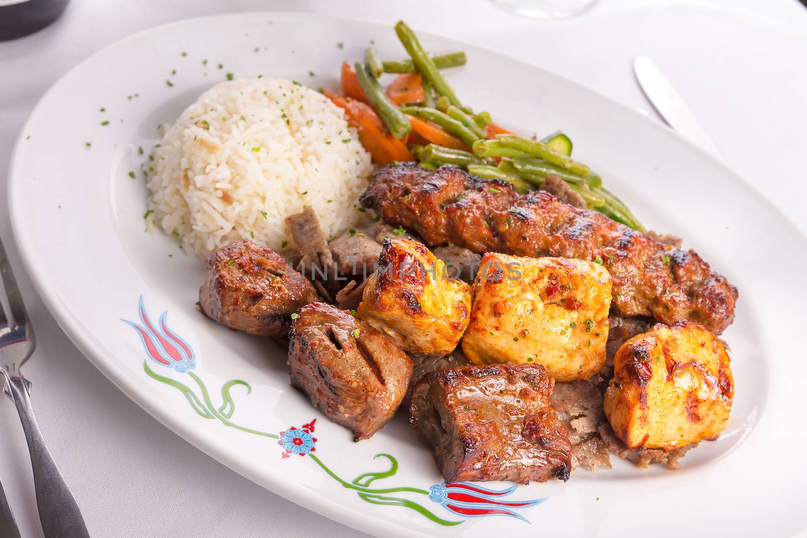 Mixed chicken, lamb adana shish kebabs served served on gyro doner with rice pilaf and garnished with green vegetables,