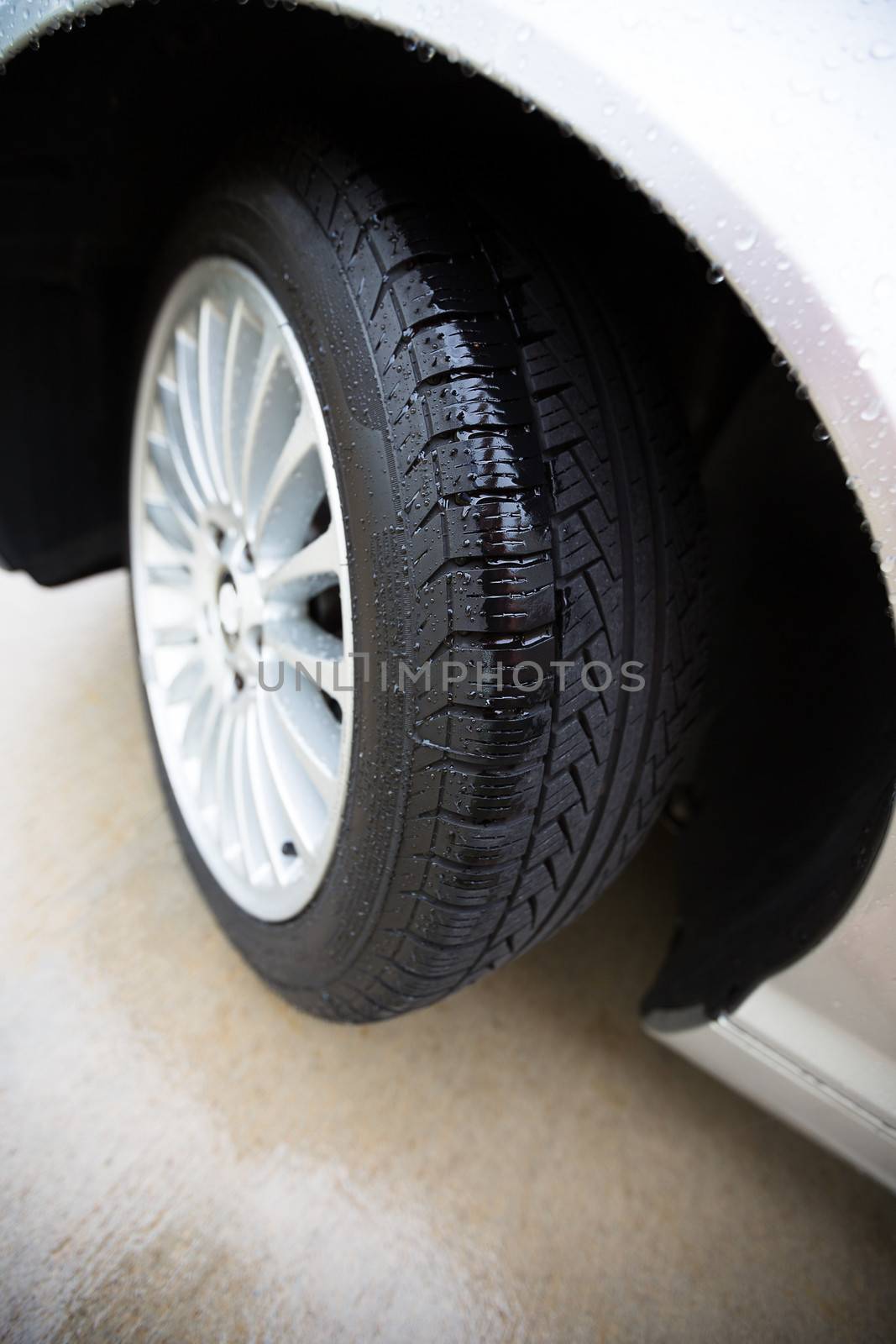 Wet automobile tire, on a concrete pavement, treads are showing clearly with rain in them