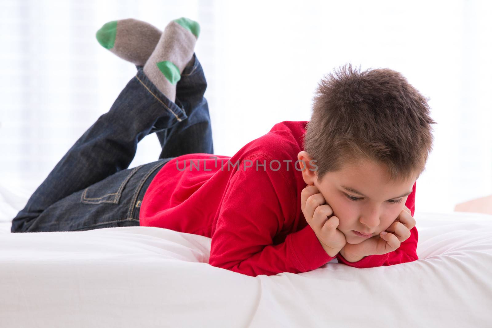 Unhappy kid looking down in the bed with his red sweater and blue jean