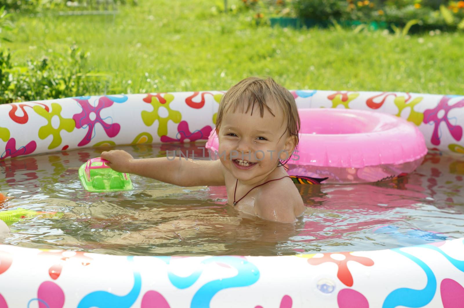 Two-year-old girl bathes in inflatable paddling pool and laughs          