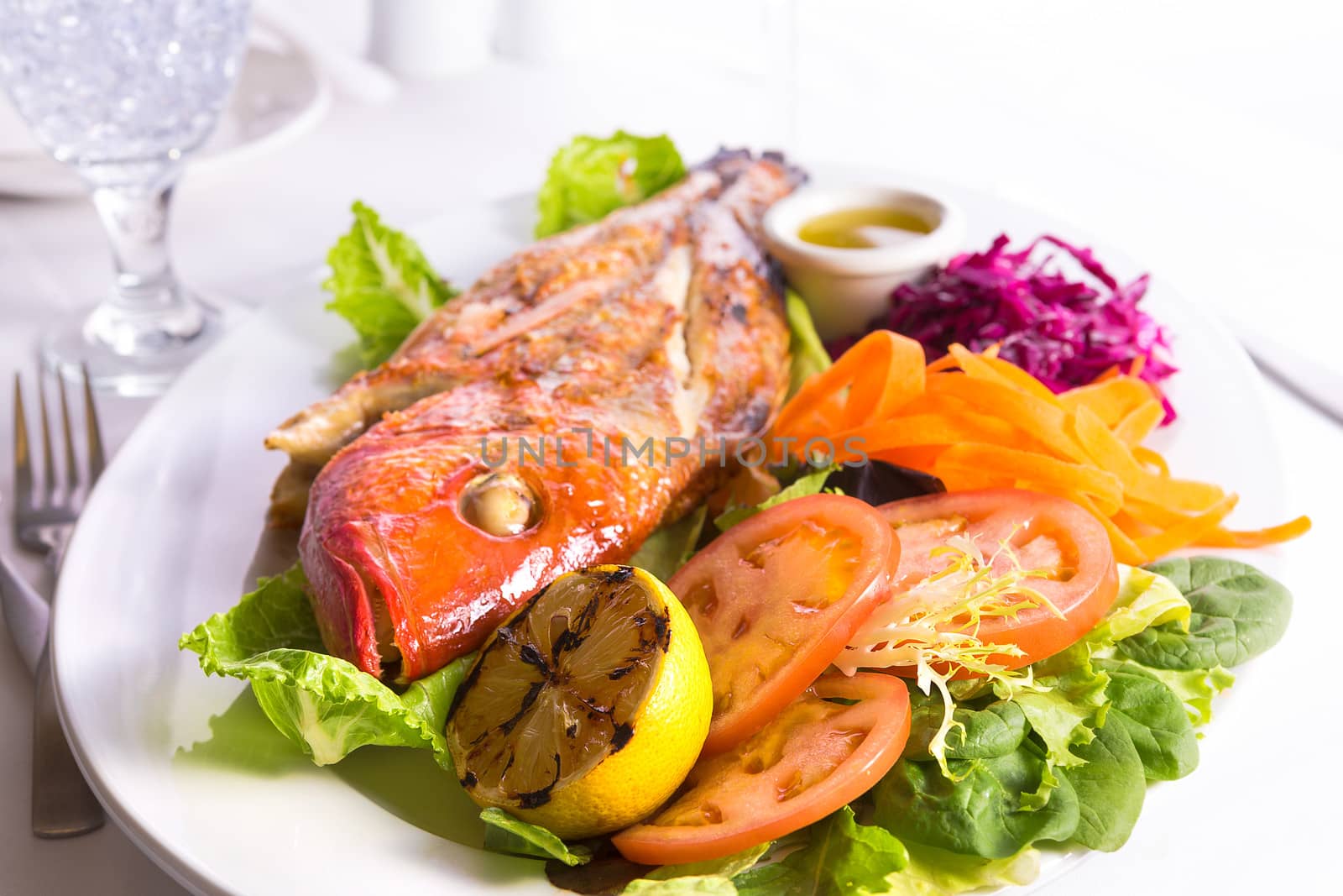 Full cooked tilapia fish served in a plate with vegetables and fish sauce complimented with Ice Water