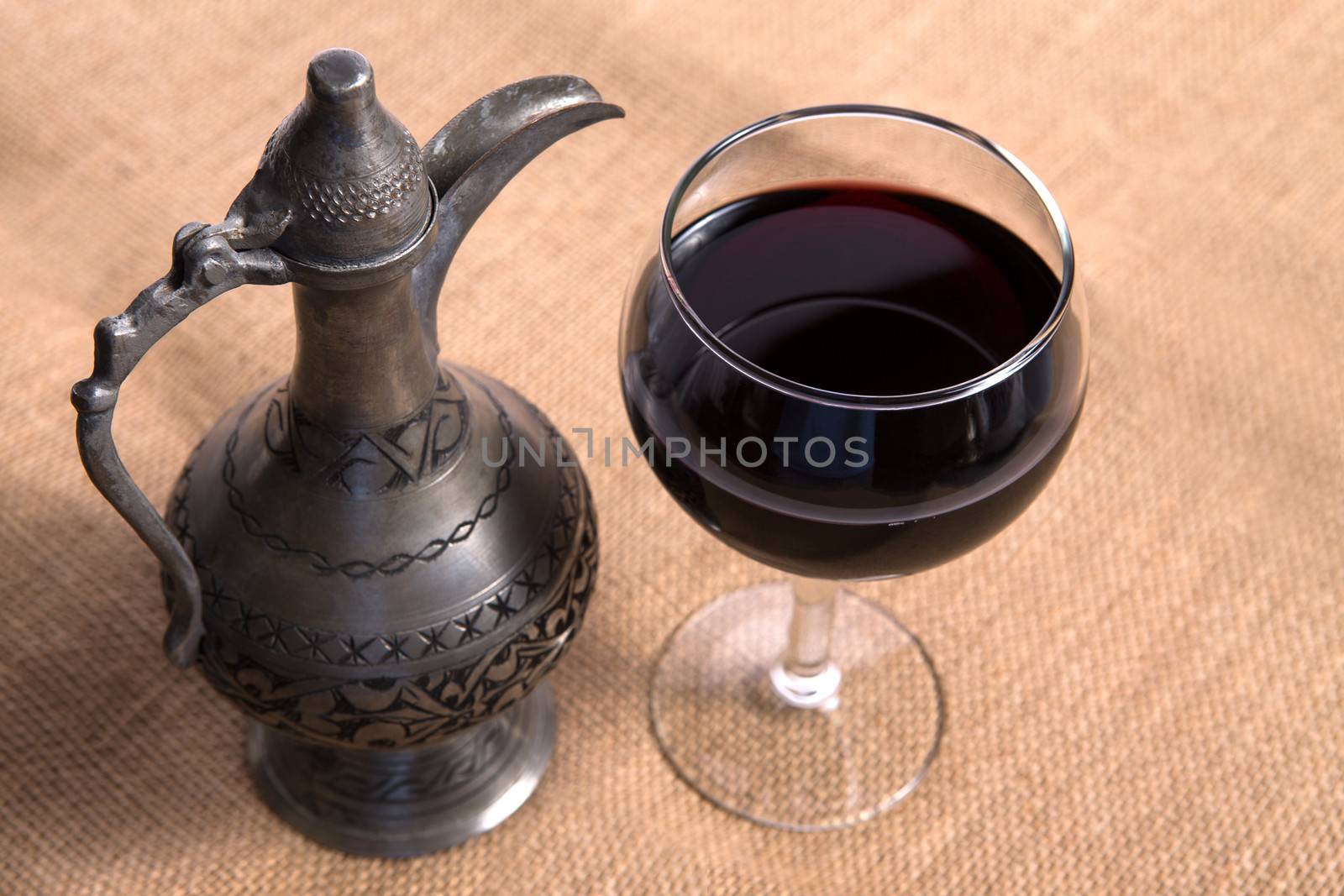 Simple View of pewter flagon and red wine in the glass on the burlap fabric