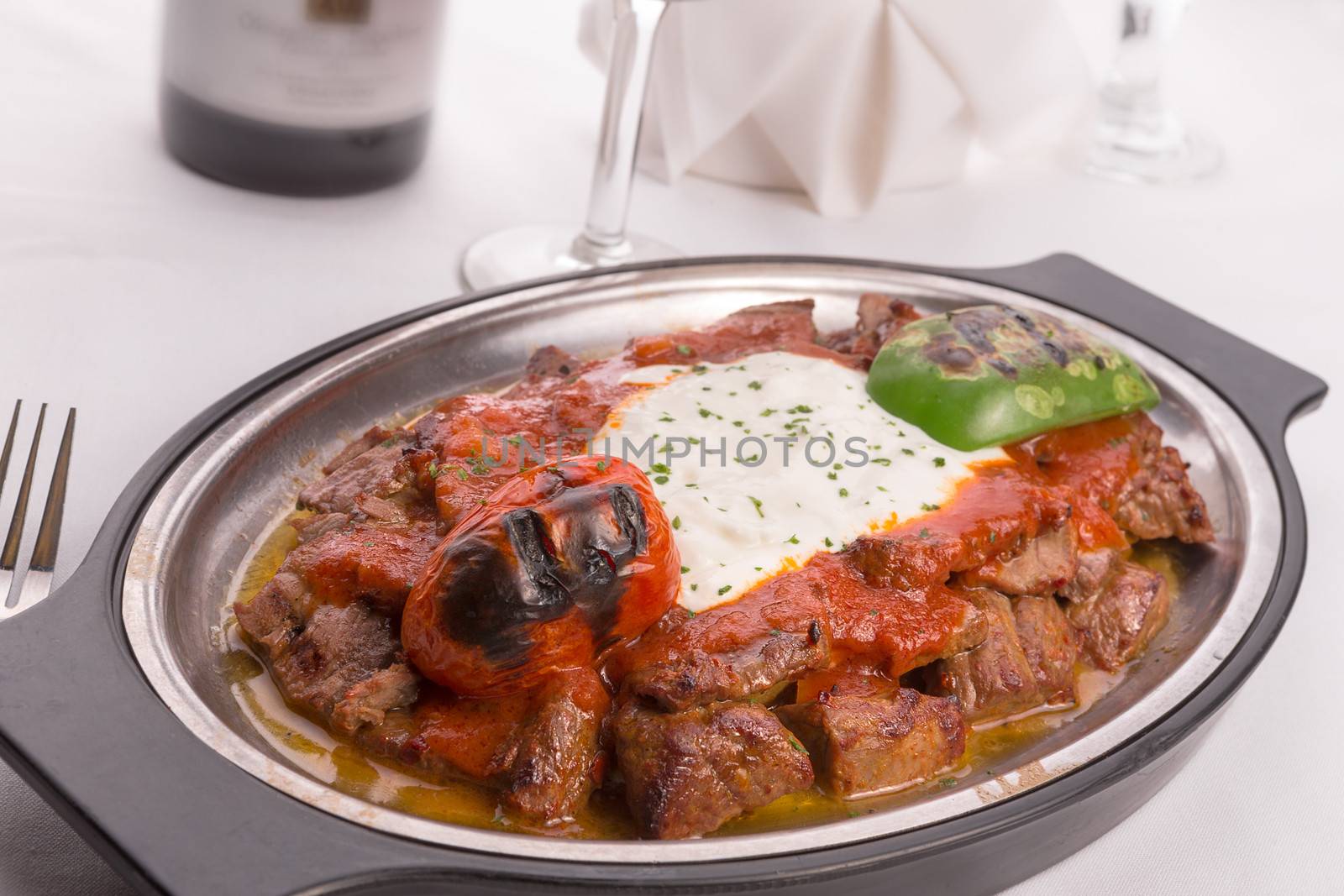 Traditional Turkish Bursa iskender kebap doner served with special red sauce and yogurt in the middle, garnished with grilled tomatoes and peppers