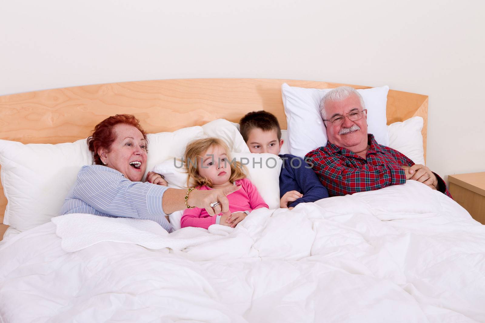 Grandparents watching TV in the bed with their grand kids, they look excited, perhaps its an adventure movie