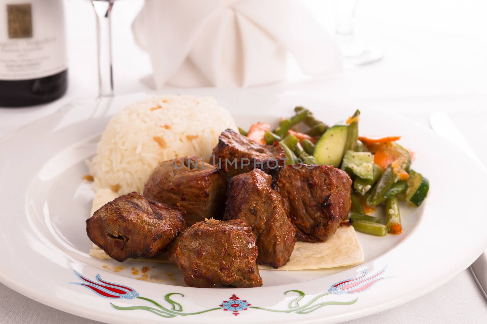 Macro shot of shish kebabs garnished with vegetables and rice pilaf, napkin and vine glass on the background