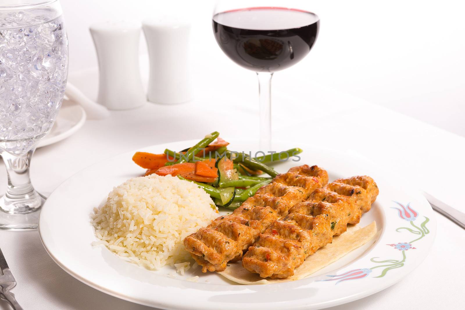 Chicken Adana kebap served with rice pilaf and green vegetables and some carrots, complimented with red Vine and ice water