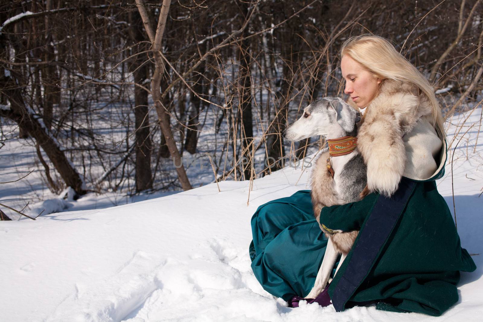 A blonde girl and a grey saluki on snow
