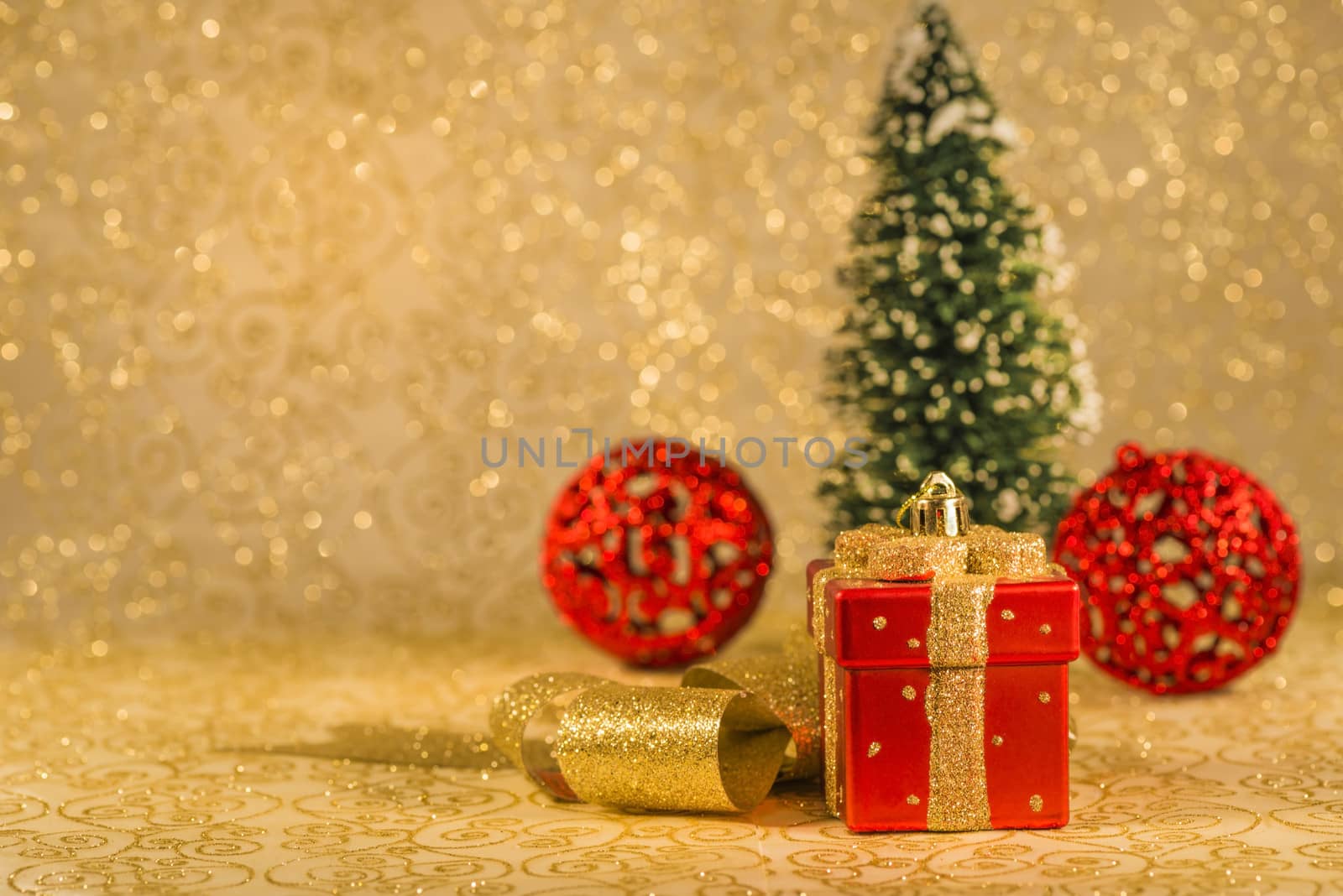 Red Christmas ornaments, golden ribbon and snowed Christmas tree on golden background