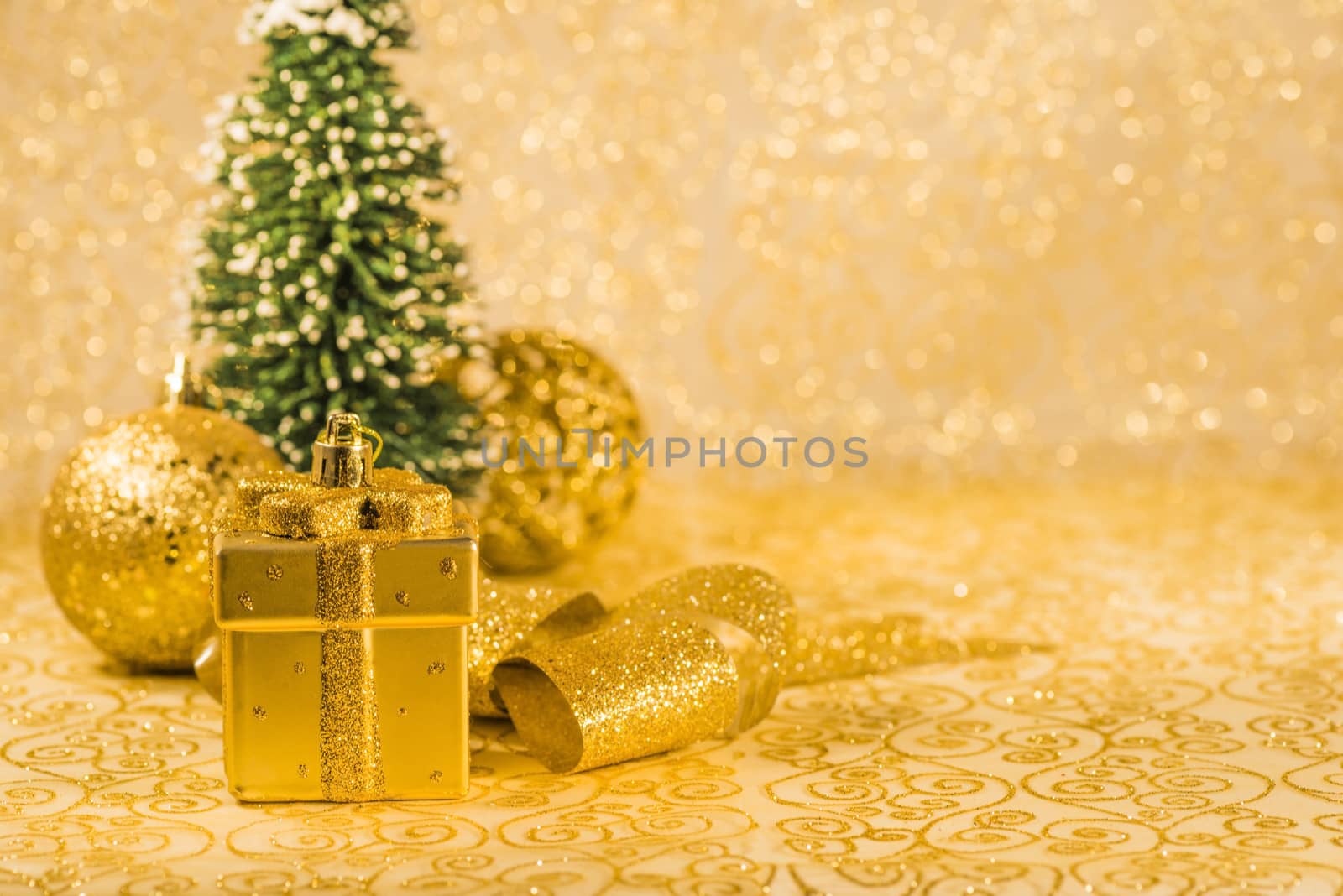 Golden Christmas ornaments, golden Christmas decoration in present box shaped, golden shiny ribbon and snowed Christmas tree on golden background
