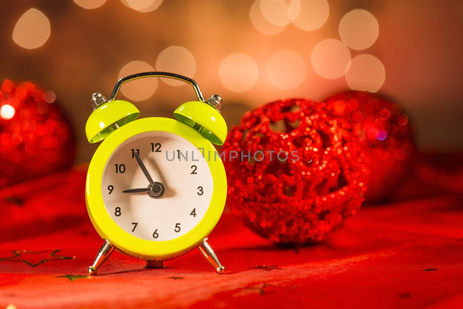 Green alarm clock and Christmas ornaments with light blur background