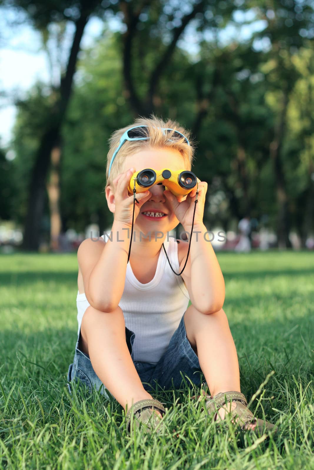 Little boy sitting in the park with a binoculars by dedmorozz