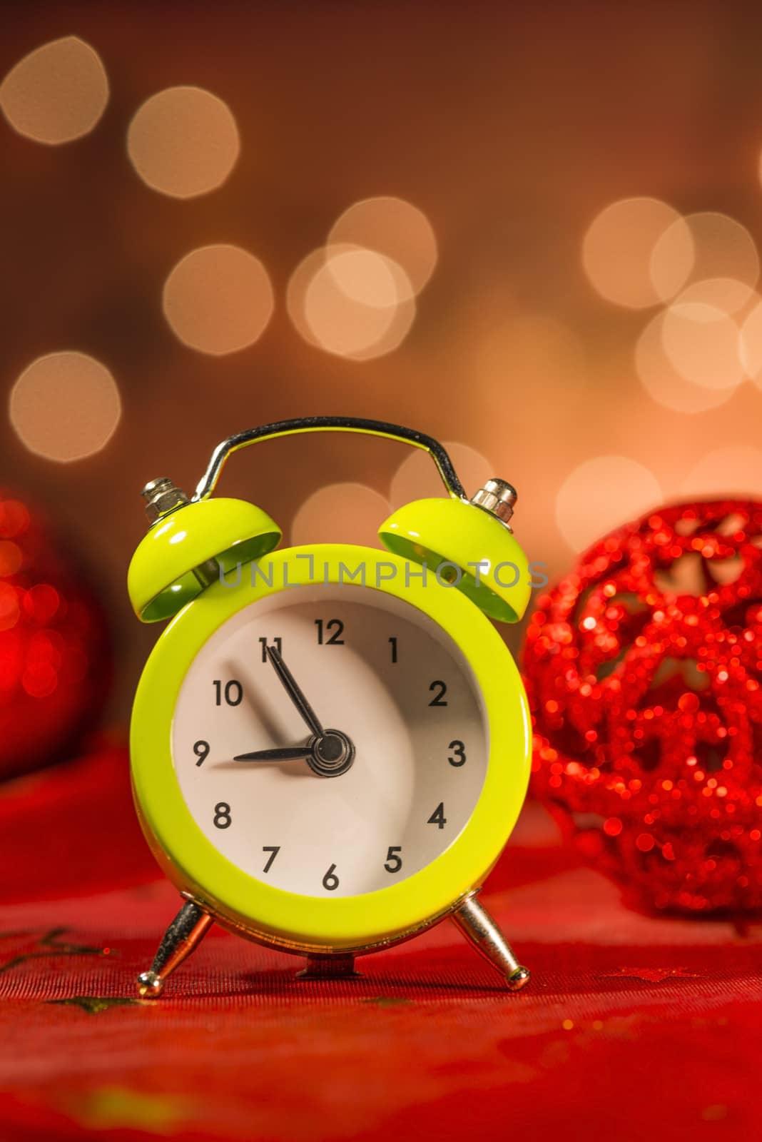 Green alarm clock and Christmas ornaments with light blur background
