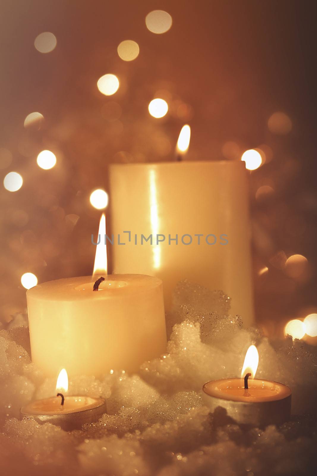 Burning candles in snow against sparkly background 