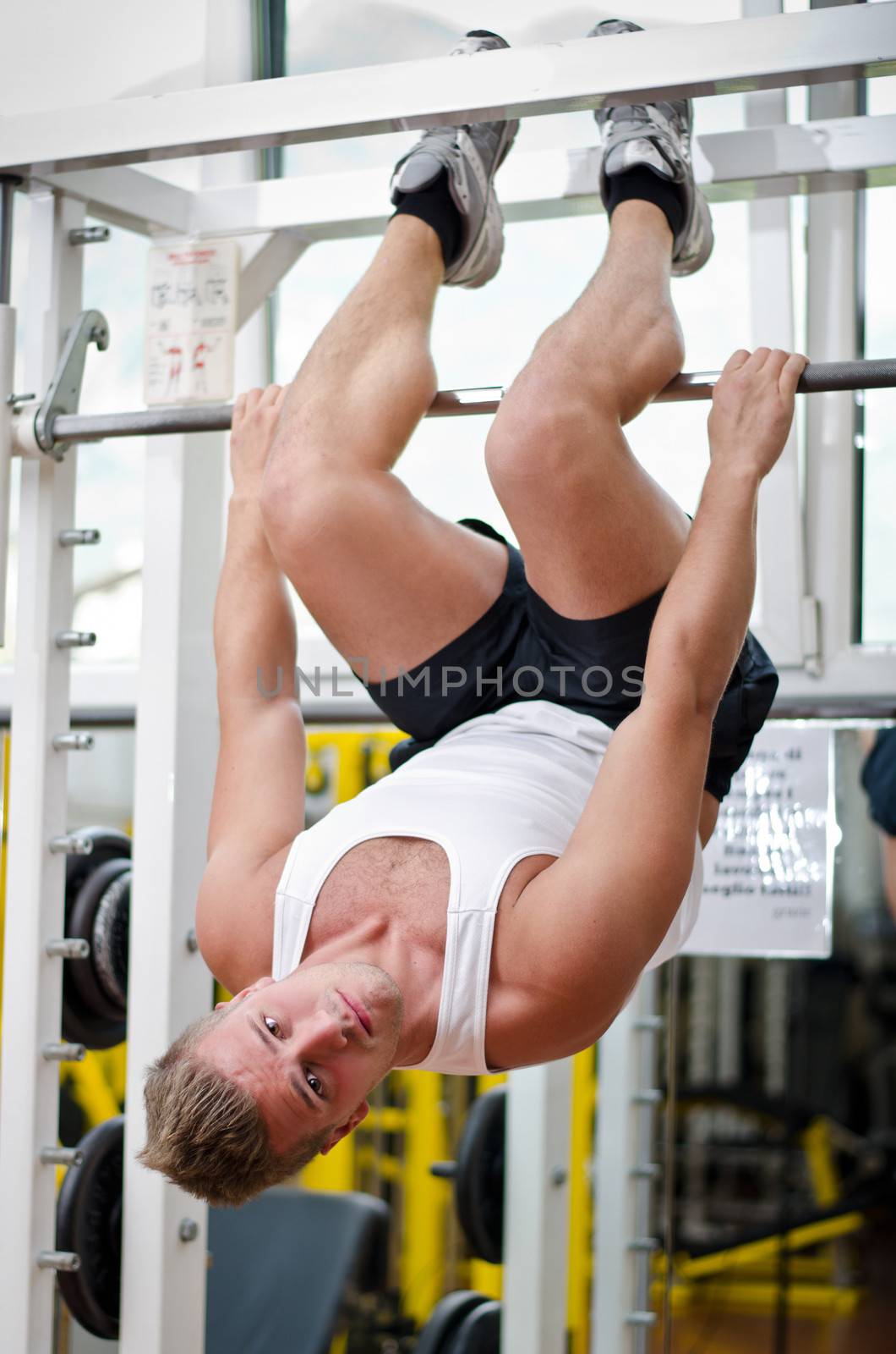 Young man in gym working out, exercising abs by hanging upside-down