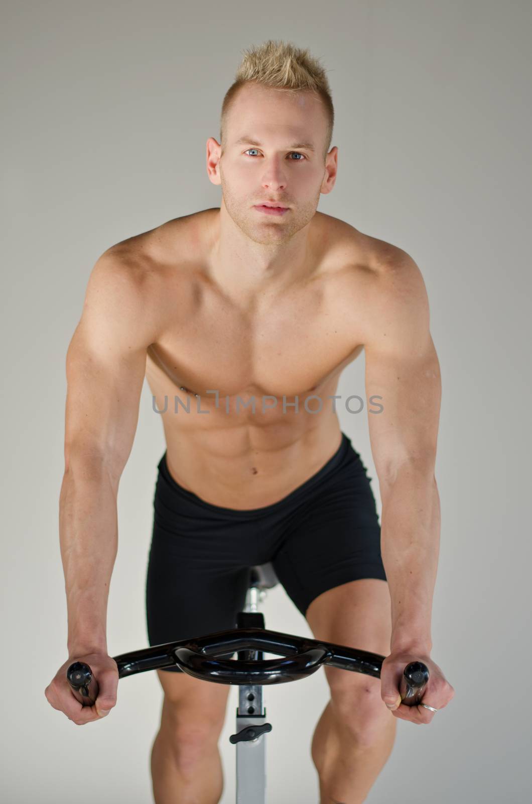 Attractive young man exercising in gym: spinning on stationary bike