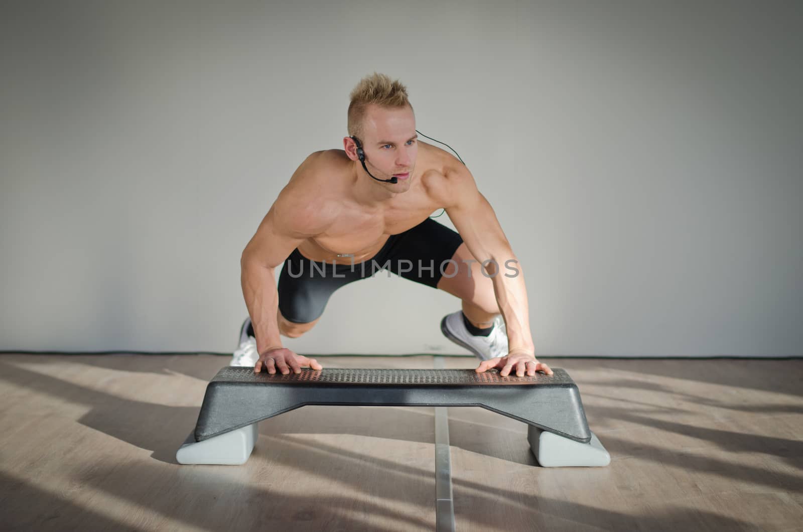 Young aerobics male coach shirtless leaning on step teaching class