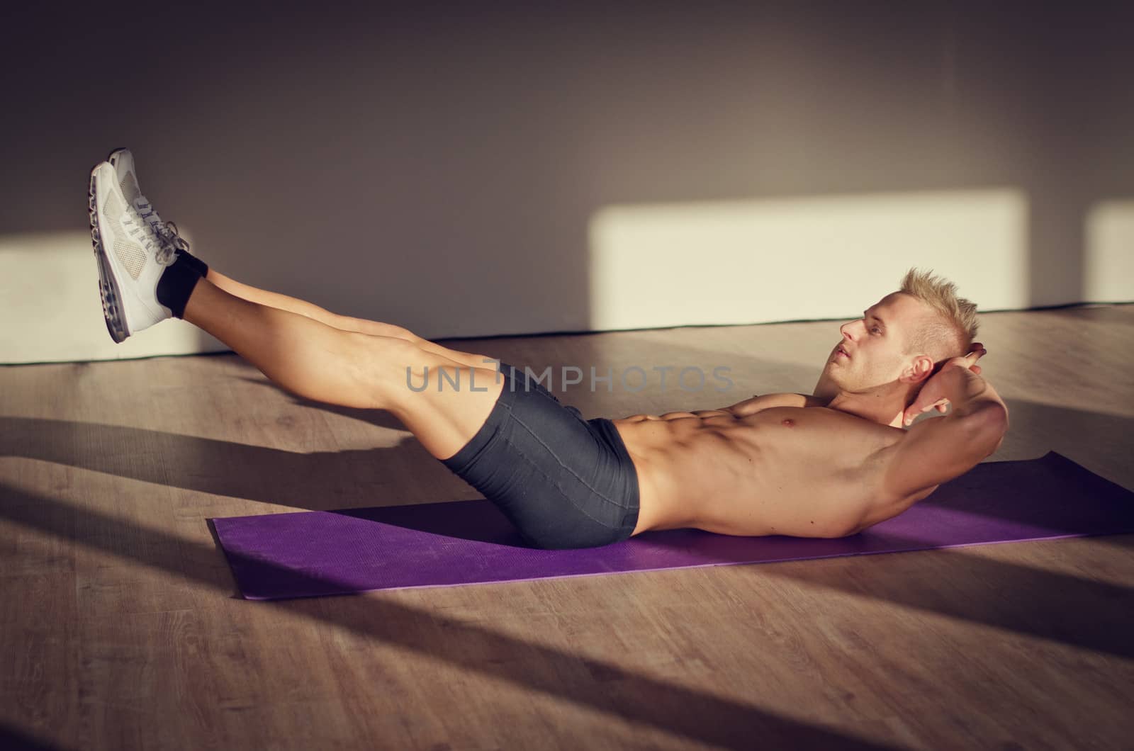 Attractive blond young man shirtless in gym working out, doing exercises for abs
