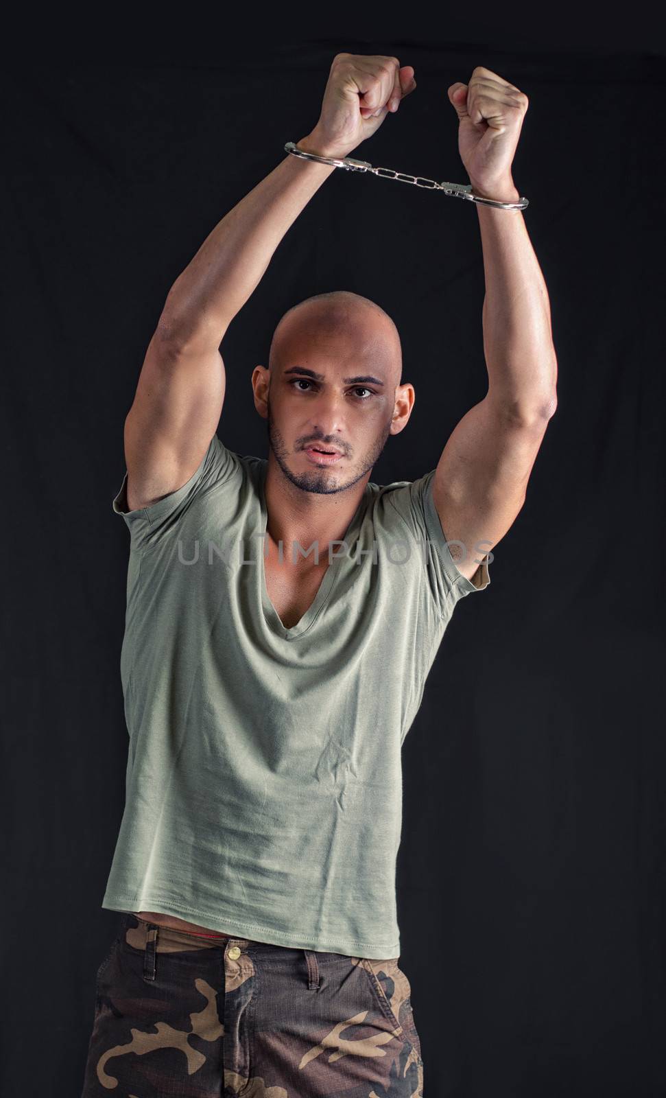 Bald young man with handcuffs, holding arms up in the air, on dark background