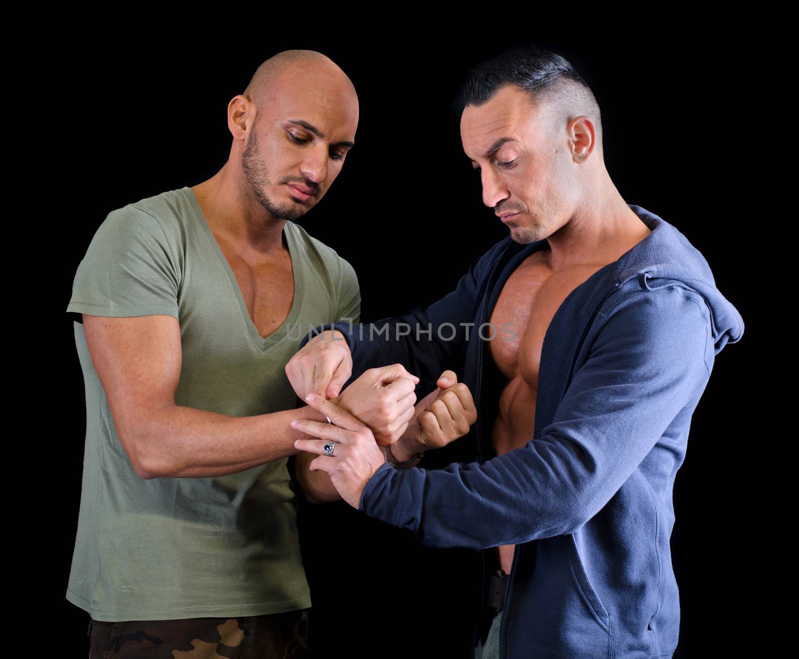 One muscular man putting handcuffs to another young man, dark background