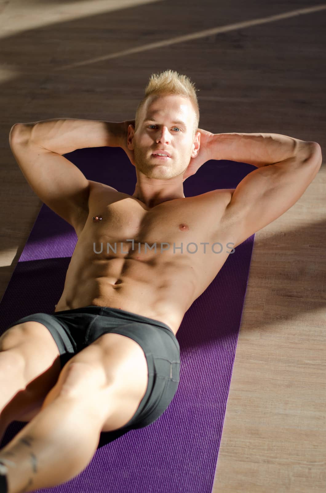 Attractive blond young man shirtless in gym working out, doing exercises for abs