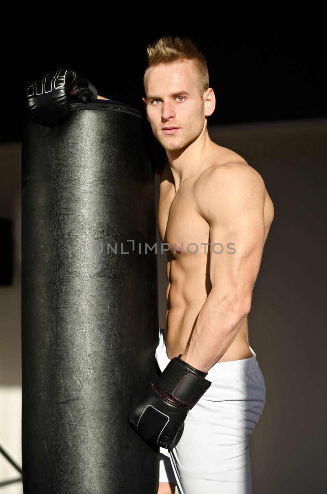 Attractive shirtless young man with boxing gloves, looking at camera