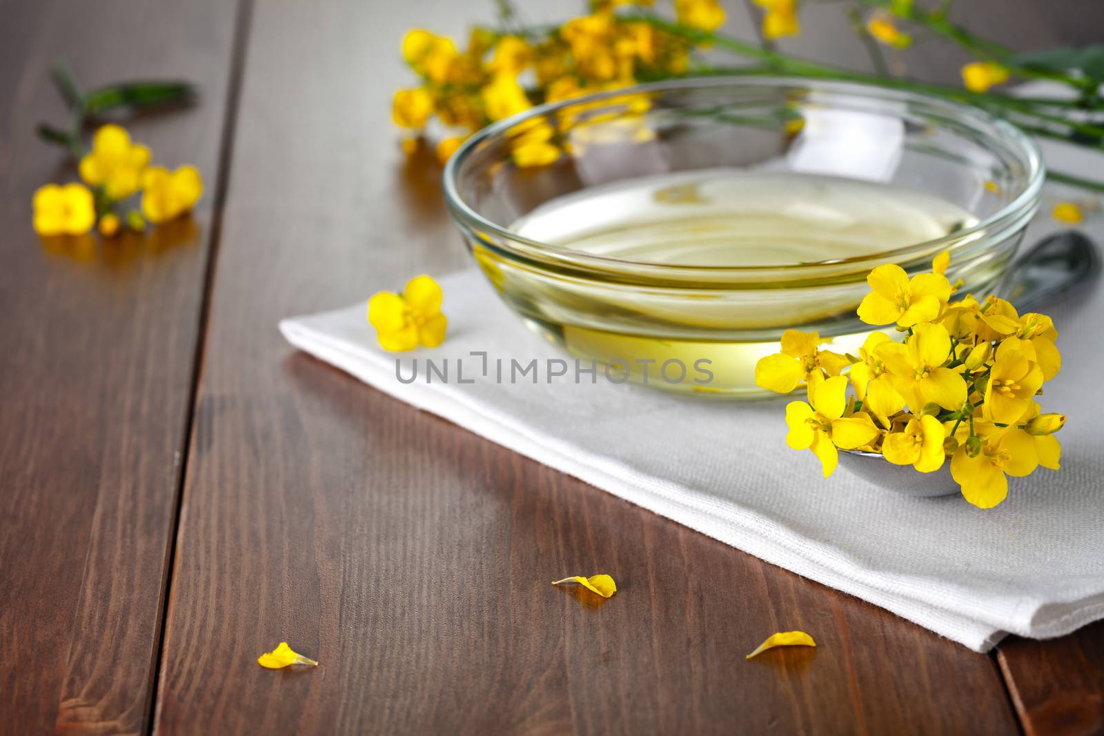 Rapeseed oil and flowers on wood background. Food composition