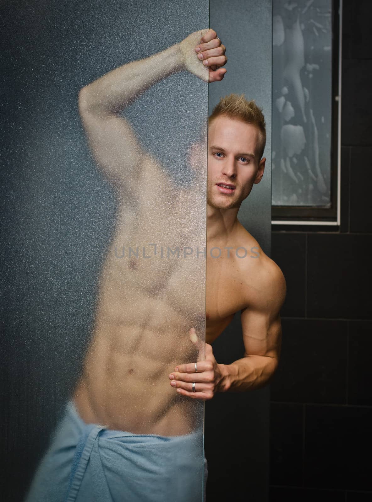 Handsome young man shirtless behind shower glass, with towel around waist