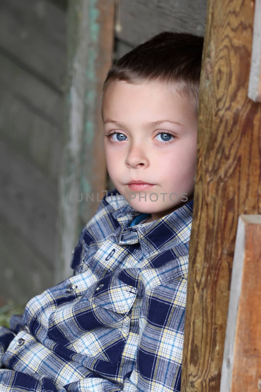 Beautiful blond boy sitting against barn wall
