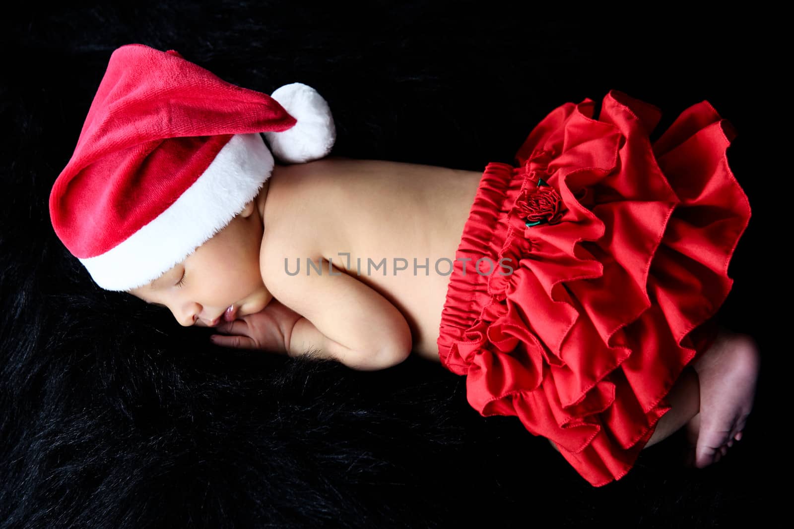 Newborn baby girl wearing a christmas hat and red frills