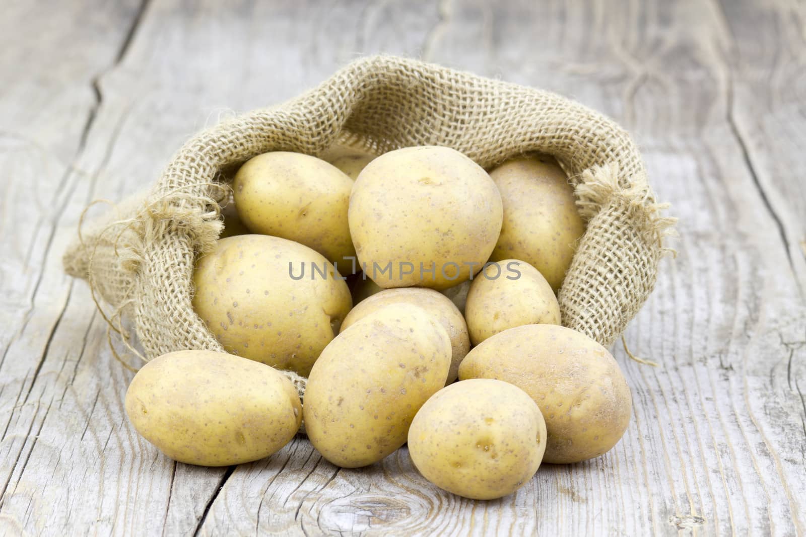 Raw potatoes in burlap bag on wooden background