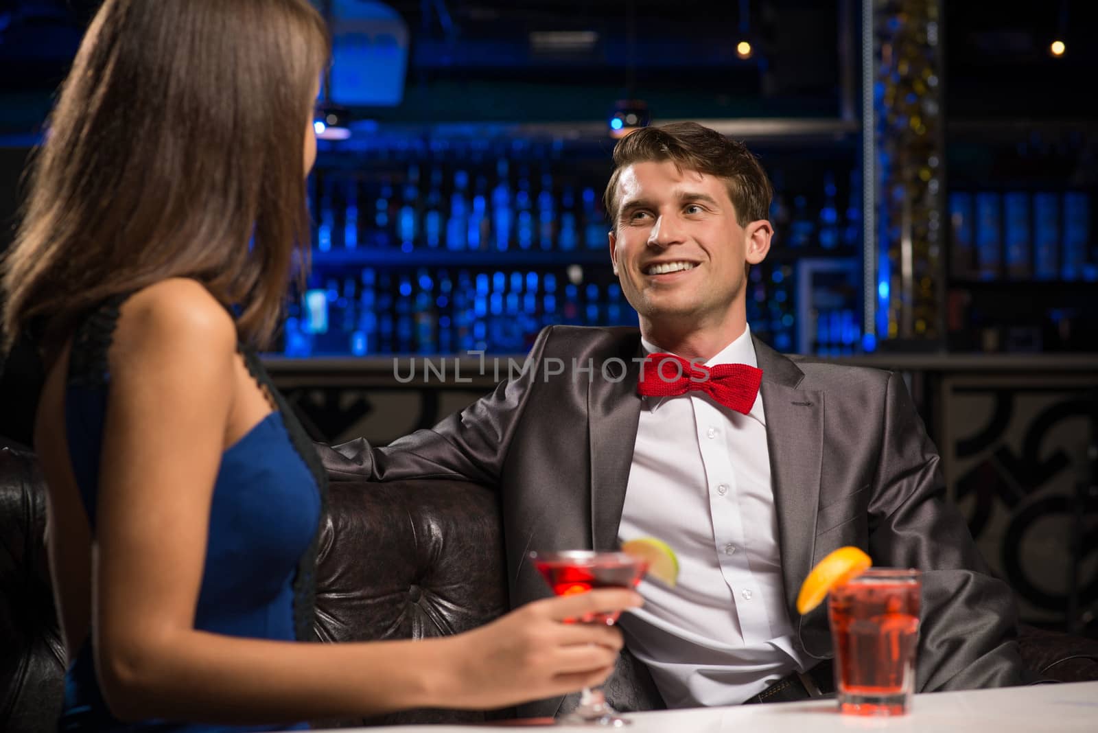 portrait of a man in a nightclub, sitting on the couch and talking with woman