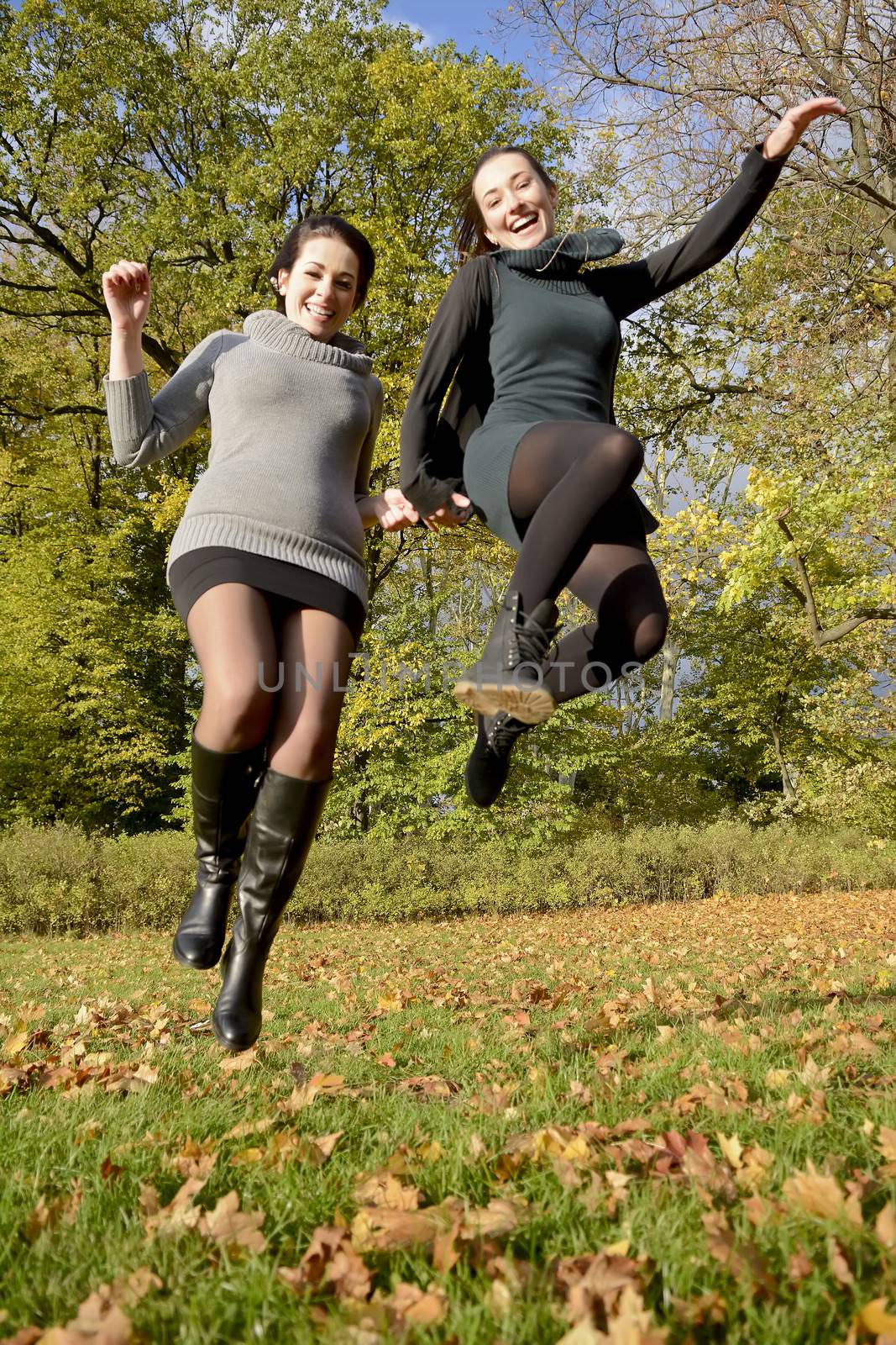  laughing sisters jumping in autumn park