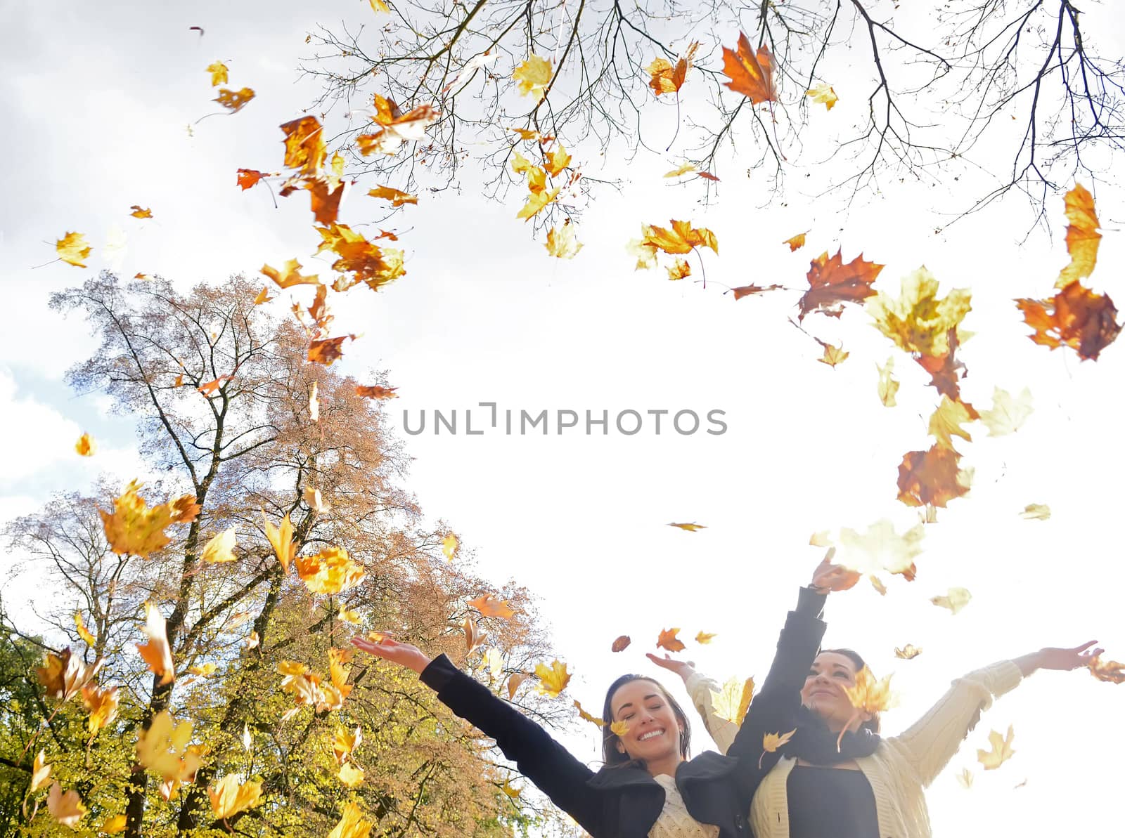  happy sisters throwing autumn leaves
