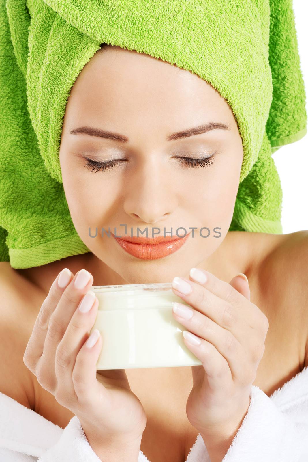 Beautiful woman in bathrobe and turban smelling body lotion. Isolated on white.