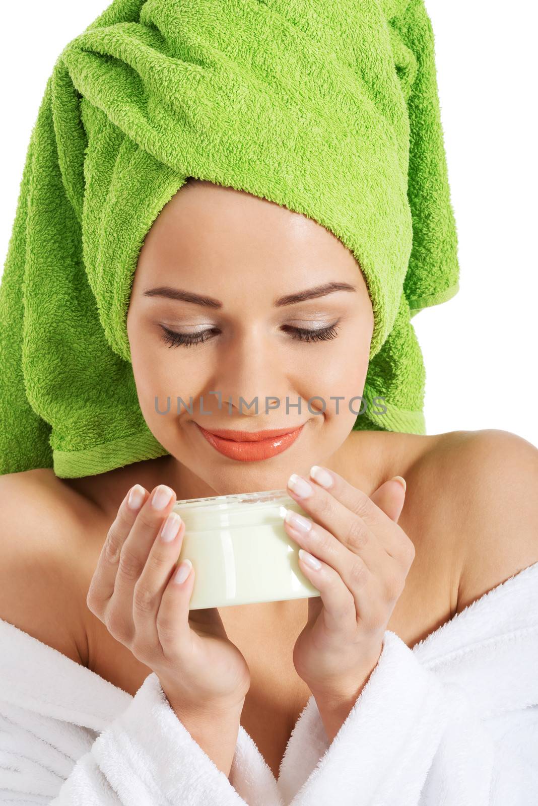 Beautiful woman in bathrobe and turban smelling body lotion. Isolated on white.